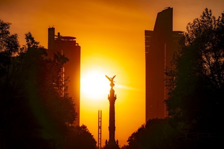 Angel de la Independencia statue in between two buildings, illuminated by the sun at sunset.
