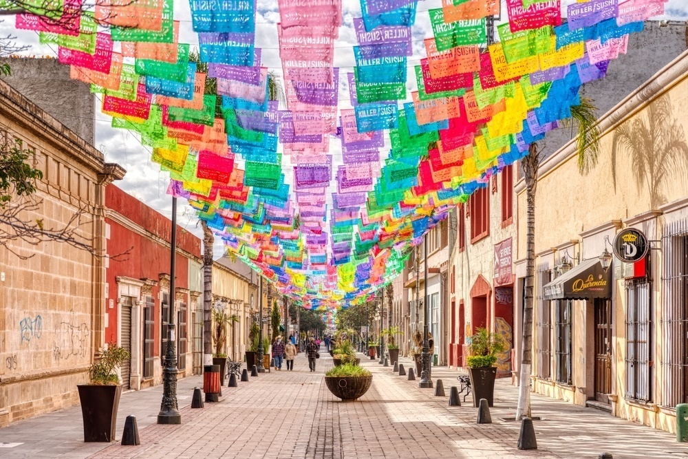 Calles coloniales del Centro Histórico, en un día soleado, con clásicos banderines mexicanos de colores colgando entre edificios.