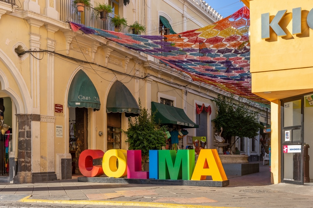 Colorido cartel de Colima en una calle peatonal del centro histórico, con banderines de colores colgando entre los edificios.
