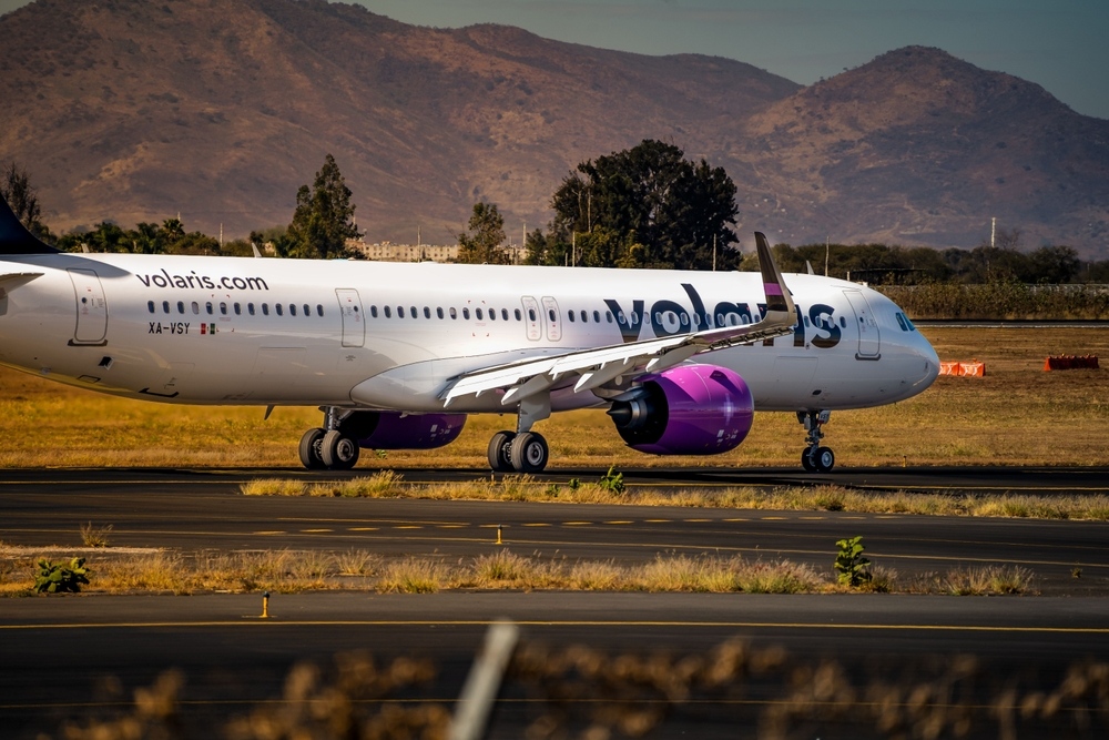 Avión de Volaris en la pista de aterrizaje del aeropuerto, con montañas de fondo.