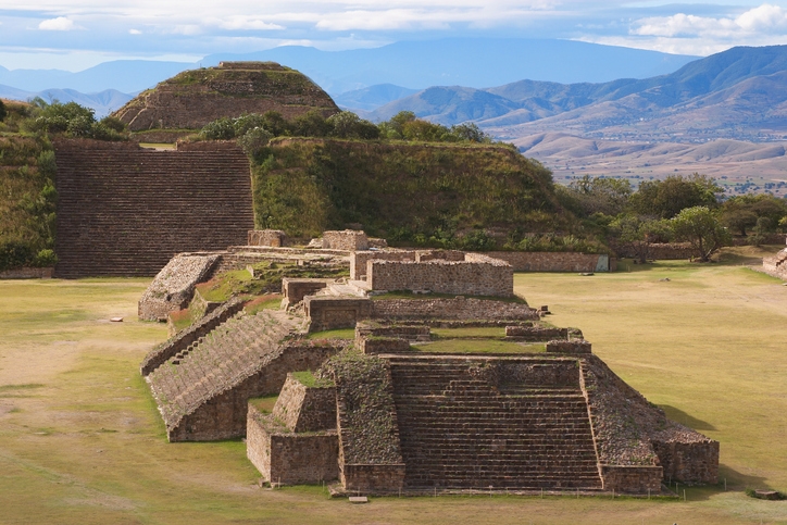 Zona arqueológica de Monte Albán con pirámides escalonadas y montañas al horizonte.