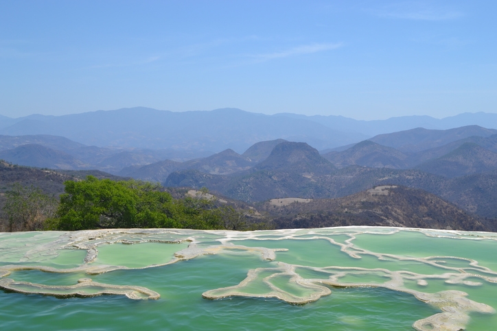 Formaciones minerales y pozas naturales en Hierve el Agua con montañas al fondo.