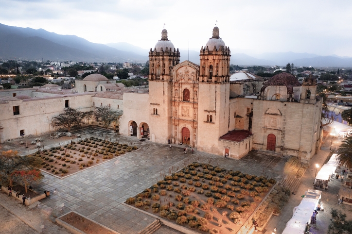 Vista aérea del Templo de Santo Domingo de Guzmán en Oaxaca, rodeado por un jardín de cactáceas.