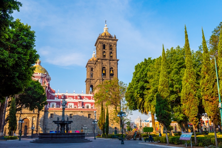 Catedral de Puebla vista desde el Zócalo, rodeada de árboles y arquitectura virreinal.