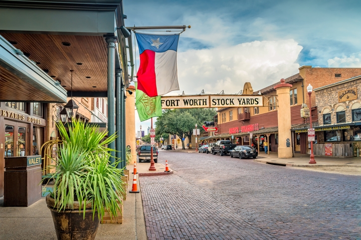 Entrada a Fort Worth Stockyards en Texas, con calles empedradas, edificios históricos y la bandera del estado ondeando en el centro.