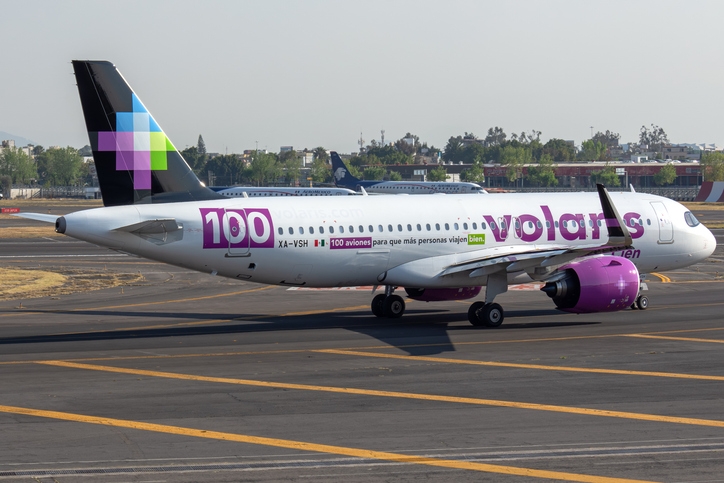 Avión de Volaris en pista, con el logo y el mensaje "100 aviones para que más personas viajen bien".