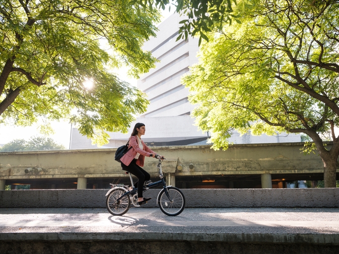 Mujer jóven andando en bicicleta por una zona de puentes y edificios.